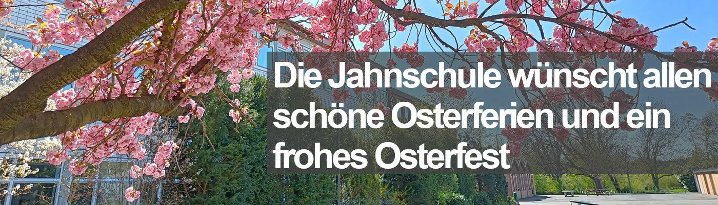 Das Bild zeigt einen rosa blühenden Zierkirschenbaum vor einem Schulhaus aus den 1960er Jahren. Darüber liegt der Text "Die Jahnschule wünscht allen schöne Osterferien und ein frohes Osterfest"